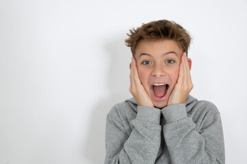 cool young 12 year old boy with grey hoody sweater posing in front of white background, having fun