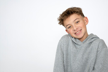 cool young 12 year old boy with grey hoody sweater posing in front of white background, having fun