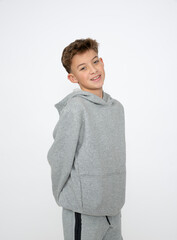 cool young 12 year old boy with grey hoody sweater posing in front of white background, having fun