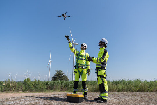 Male engineer using and control drone for inspection quality of engine of wind turbine at wind turbine farm area. Group of male technician working and planning maintenance of wind turbines at windmill