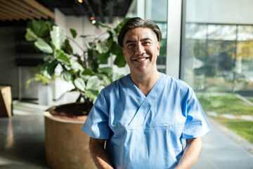 Smiling healthcare professional portrait in scrubs with arms crossed in hallway