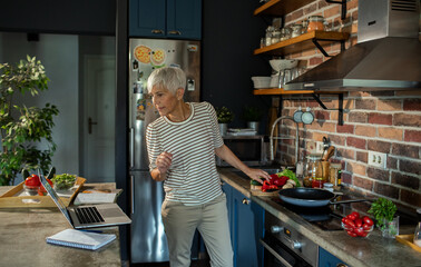 Senior woman preparing healthy meal in modern kitchen with fresh vegetables
