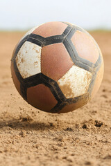 dusty football bouncing on dirt field, kicking up particles as it moves. worn texture and colors of ball highlight its use in outdoor play