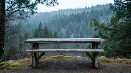 Fototapeta premium Weathered wooden picnic table in front of a tranquil forest scene with misty mountains and lush trees in the background