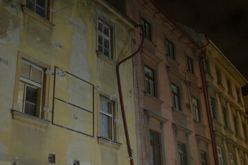 Fototapeta premium The breathtaking view of the night showcases two historic building facades that feature intricate details and visible utility pipes, all set against a lively and vibrant urban backdrop