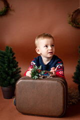 beautiful boy child 3 years old on brown background with christmas tree and an old suitcase