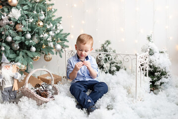 Cute handsome boy 3 years old sitting near Christmas tree eating candy