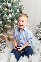 Cute handsome boy 3 years old sitting near Christmas tree eating candy
