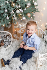 Cute handsome boy sitting under Christmas tree at home and eating  bar of chocolate.