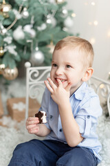 Cute handsome boy 3 years old sitting near Christmas tree eating candy