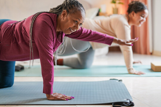 African mother and daughter doing yoga class together at home during winter season - Sport, active lifestyle and family love concept - Focus on woman shoulder