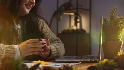 Business woman in new year decorated room sitting working at desk on laptop in home office holding...