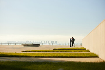 Two business professionals discussing plans on modern rooftop with city skyline in background and...