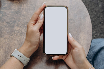 Woman's hand holding using smart phone with white blank screen at coffee shop, mobile app design...