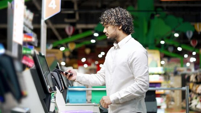 Male customer using self-service cashier checkout in a supermarket Shopper scanning produce items using at grocery store self serve cash register pos terminal man banking pay for products online