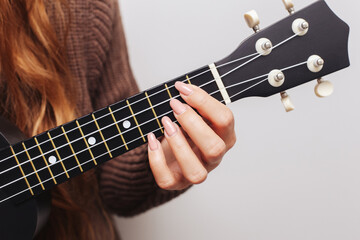 Long haired girl playing a black ukulele. Holding a chord on the fretboard with her hand. Musical...