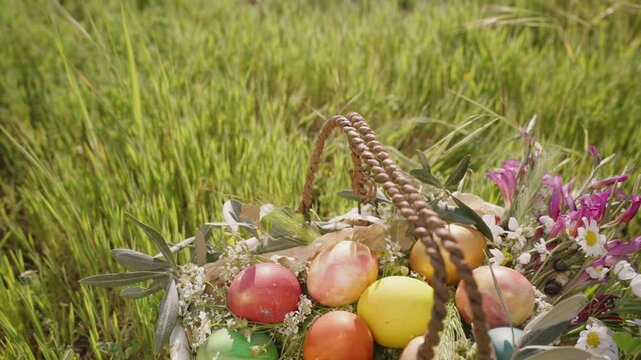 A Close-Up of a Basket Filled with Vibrant Easter Eggs and Fresh Flowers, Resting in a Lush Green Field. Slow motion.