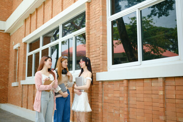 Fototapeta premium Three women are standing outside a brick building, talking and holding books