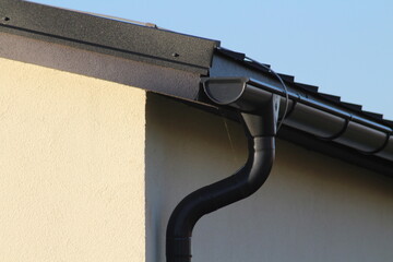 Black gutter on the side of modern white house with black metal roof and small bird sitting on top...