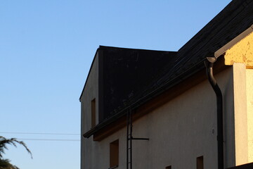 Black gutter on the side of modern white house with black metal roof and small bird sitting on top of the roof. Real estate concept
