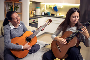 Mother and daughter playing guitar at home. A mother teaches her daughter to play the guitar.