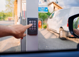 Close-up of a hand pressing a button on a keypad to open a gate, with a white van visible in the background and taken from inside a vehicle