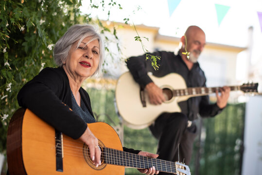 Man and woman, 65 years old, playing guitar in the Andalusian courtyard of their home