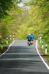 Obraz premium People riding scooters on a scenic rural road surrounded by lush green trees