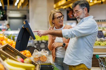 Senior couple weighing oranges on digital scale in supermarket