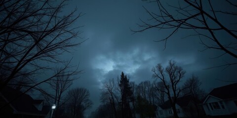 Eerie suburban scene with leafless tree branches swaying under dark clouds, night, autumn