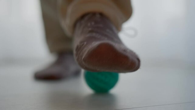 Precise foot massage with a ball.
A man rolls a ball with his foot to relieve pain.
Leg problems.
Foot massage