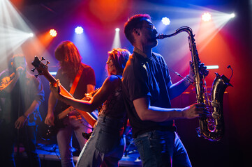 Music band playing live on stage with colorful lights, saxophonist and bassist in foreground