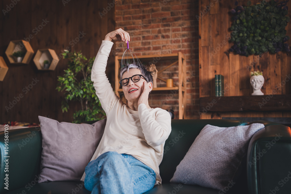 Wall mural Happy elderly woman enjoying a relaxing weekend moment indoors, wearing casual attire. Joyful mature lady with glasses