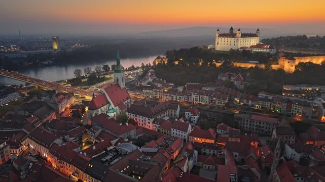 Aerial evening sunset view of Bratislava old town and Bratislava Castle or Bratislavsky Hrad. Cental part of Bratislava with city lights and orange sunset sky, Slovakia