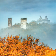 autumn landscape with ruins of castle in fog and golden leaves on foreground
