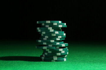 Stack of poker chips on green table against dark background, closeup