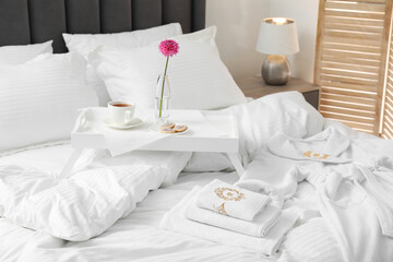 Breakfast tray, towels and bathrobe on bed with beautiful linens indoors