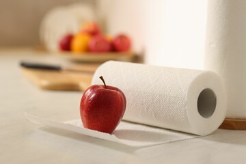 Fototapeta premium Roll of paper towels and red apple on white countertop in kitchen, closeup