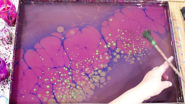 A hand throws drops of green paint onto an ebru panel
