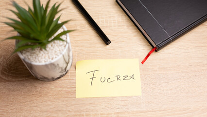 Fuerza handwritten note on yellow sticky note on wooden desk with pen, plant and notebook