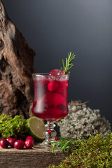 Cranberry cocktail with ice, lime, and rosemary on a old wooden board.