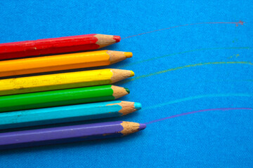 colored wooden pencils in a row, on blue background. top view