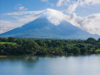 Fototapeta premium Majestic volcano towers over lush landscape and tranquil lake during bright sunny day