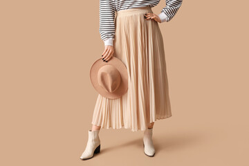 Legs of beautiful young woman wearing beige long corrugated skirt on beige background
