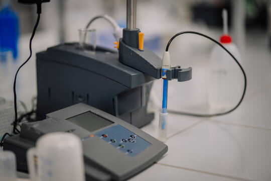 Laboratory pH meter with an attached electrode probe, used for measuring acidity levels in samples, placed on a white tile bench.