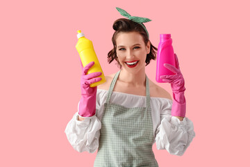 Beautiful young happy pin-up housewife with bottles detergent on pink background