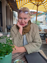 Portrait of cheerful mature woman sitting at table in street cafe, smiling at camera