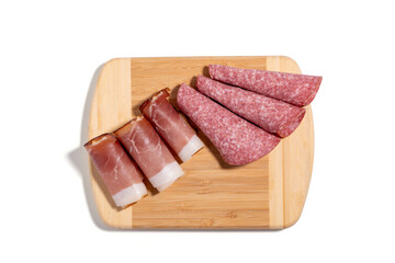 A wooden cutting board with a variety of meats on it. The meats include ham, salami, and bacon Bacon and salami isolated on white background.
