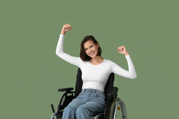 Young pretty woman in wheelchair showing strength gesture on green background