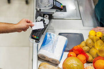 Customer paying with contactless credit card at supermarket checkout